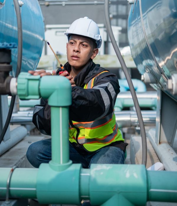 About US Focused industrial engineer using a calibration tool to check equipment at a manufacturing plant, ensuring operational efficiency.